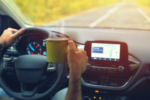 driver motorist holding a mug drink in hand while driving on the road distracted driving